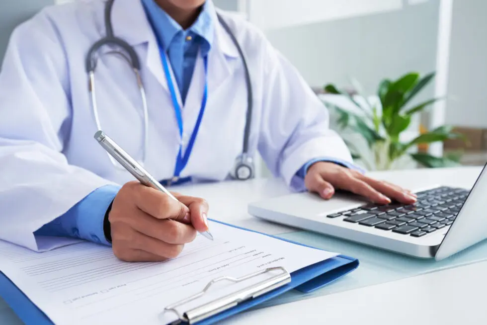 hands-unrecognizable-female-doctor-writing-form-typing-laptop-keyboard-980x654.jpg